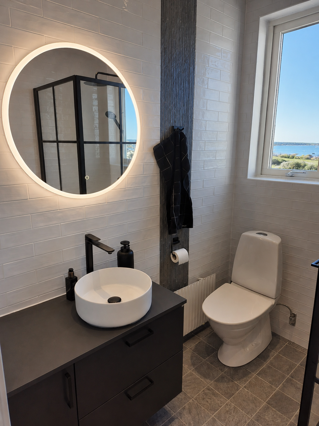 Renoverat badrum med rund LED-spegel och svarta detaljer